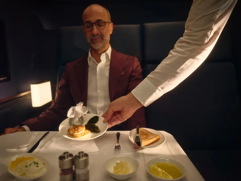 Mann in Anzug bekommt vom Kellner Teller mit Kaviar, Blini und Garnitur in elegant gedeckter Restauranttafelrunde