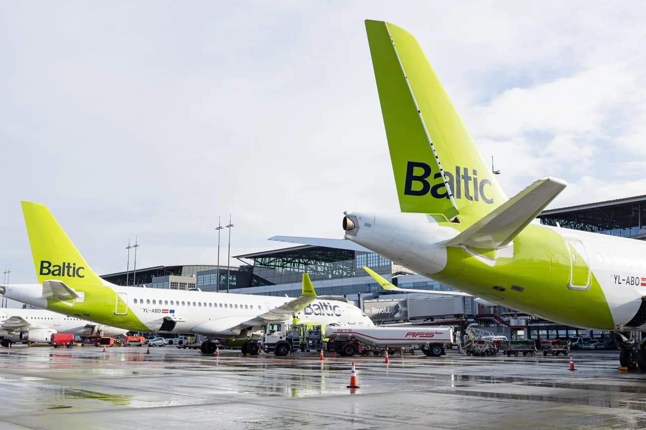 AirBaltic Flugzeuge mit markanter limegrüner Heckflosse auf nassem Vorfeld beim Betanken und Gepäckhandling vor Terminalgebäude