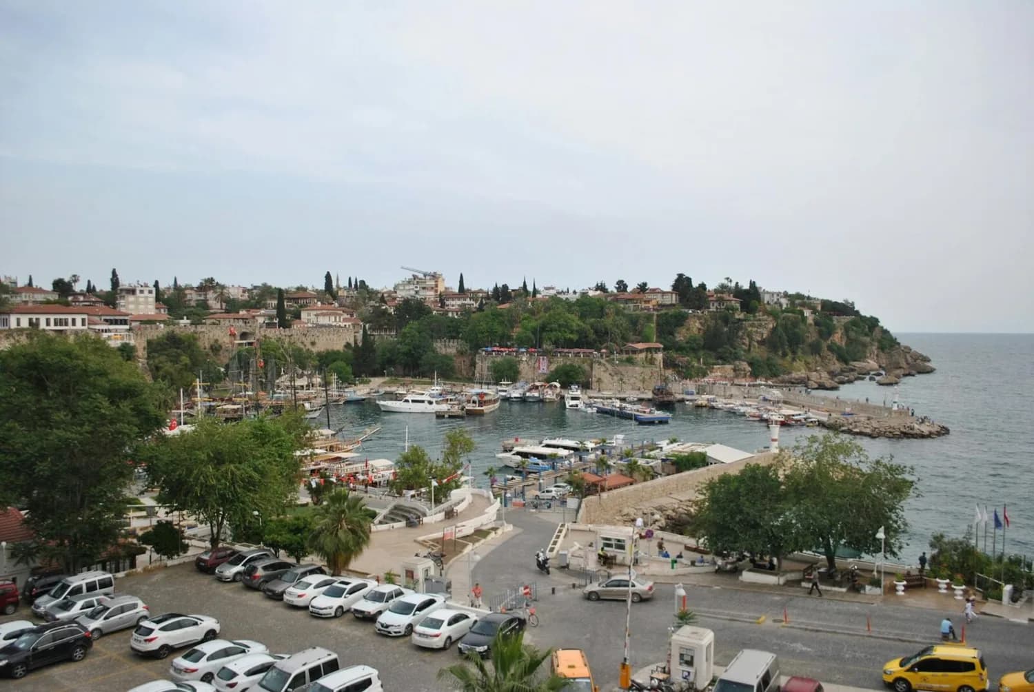 Antalya Hafen mit Booten und Yachten, Uferpromenade und historischer Küstenlage, Blick vom Parkbereich mit geparkten Autos – Flugverbindung Bremen Antalya Hinweis beachten
