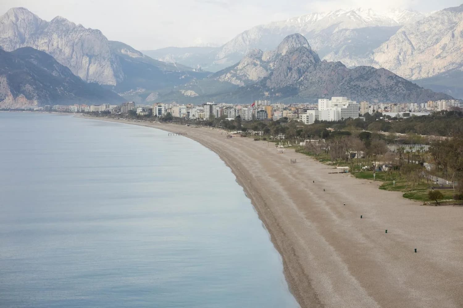 Leerer Sandstrand von Antalya mit ruhigem Meer, Küstenpromenade, Hotels und Stadt vor schroffen Taurusbergen – Antalya Flug ab Düsseldorf relevant für Urlaubszielbeschreibung
