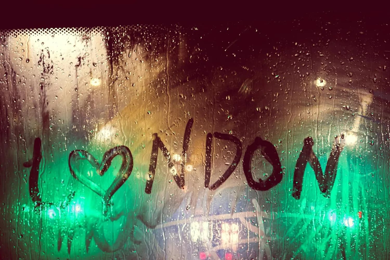 von innen beschlagene Autoscheibe mit handgeschriebener Aufschrift I ♥ NDON, Regentropfen und verschwommene Straßenlichter in London/Düsseldorf