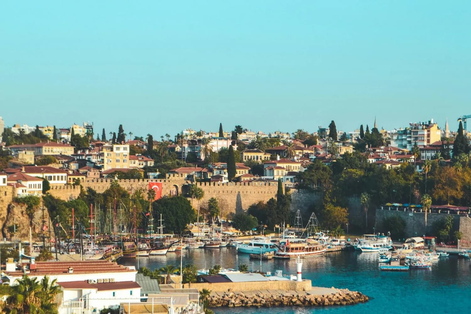 Antalya Hafen mit Booten vor historischer Stadtmauer und Häusern, türkische Flagge sichtbar, Urlaubs- und Flugziel von Düsseldorf aus