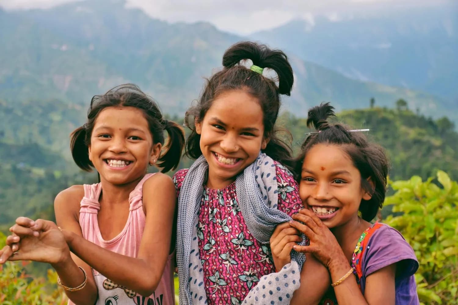 Drei lachende Kinder in bunten Kleidern vor Berglandschaft, freundschaftliche Szene für easyJet Easter Collection und UNICEF Kinderaktion