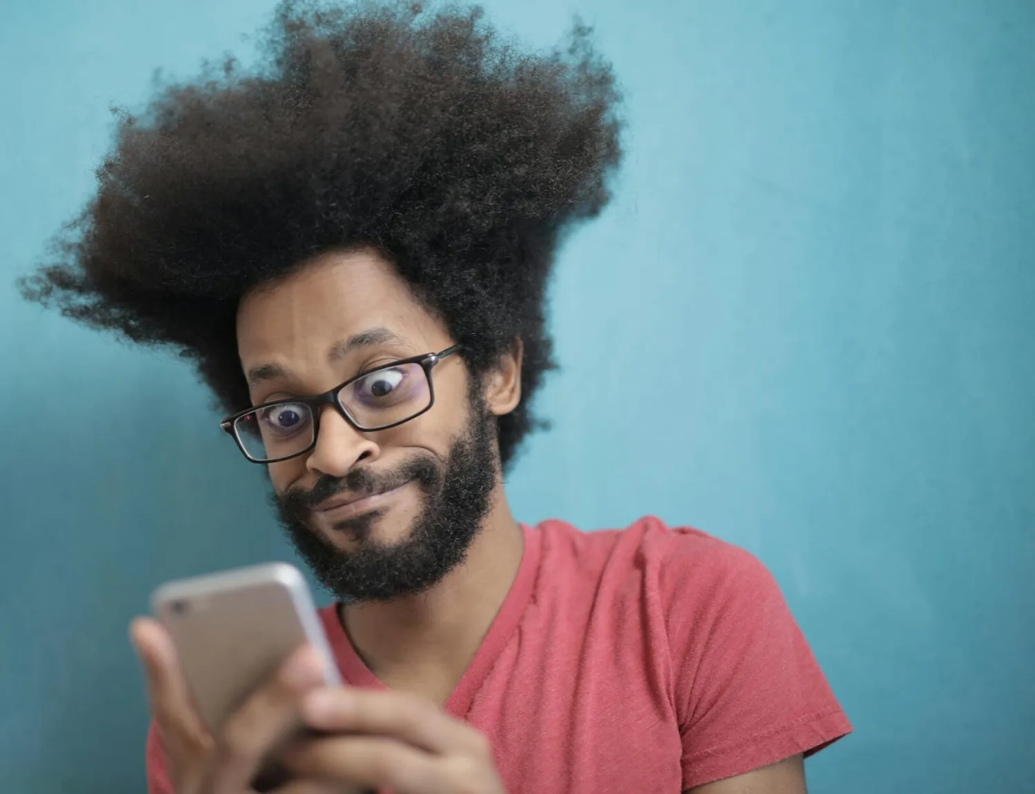 Mann mit Afro und Brille liest überrascht auf Smartphone vor türkisfarbenem Hintergrund, reaktionsstarke Gesichtsausdrucksaufnahme, Aena Gruppe Rekordzahlen-Kontext