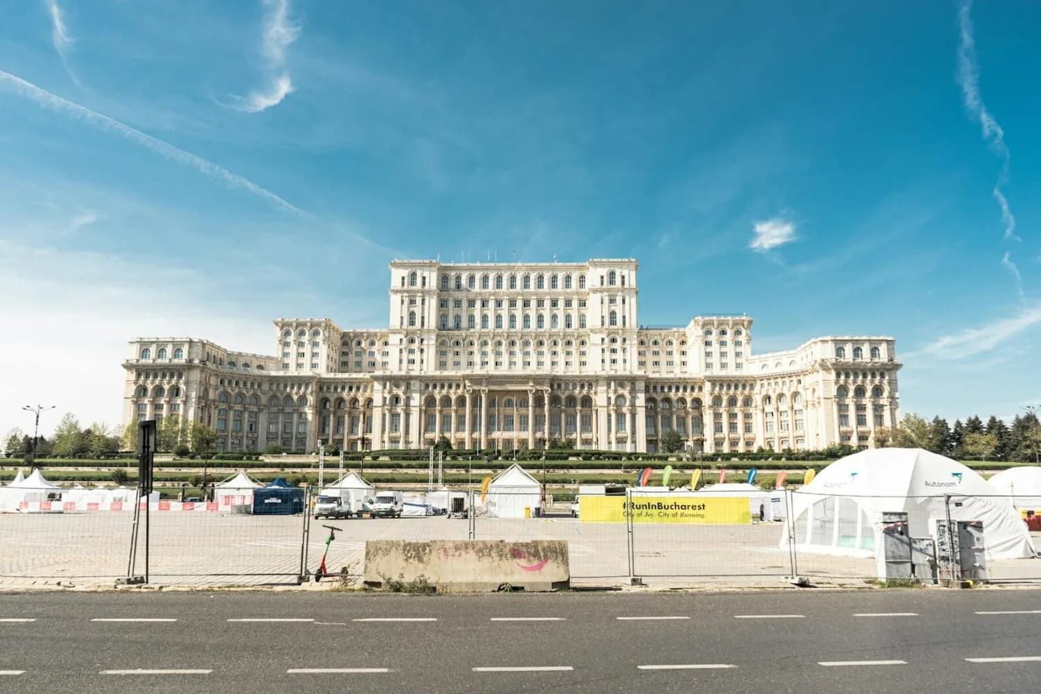 Parlamentspalast von Bukarest vor blauem Himmel, Veranstaltungszelte und Absperrungen im Vordergrund, städtische Szenerie zwischen Bukarest und Karlsruhe Flugverbindung relevant für Reisecontent