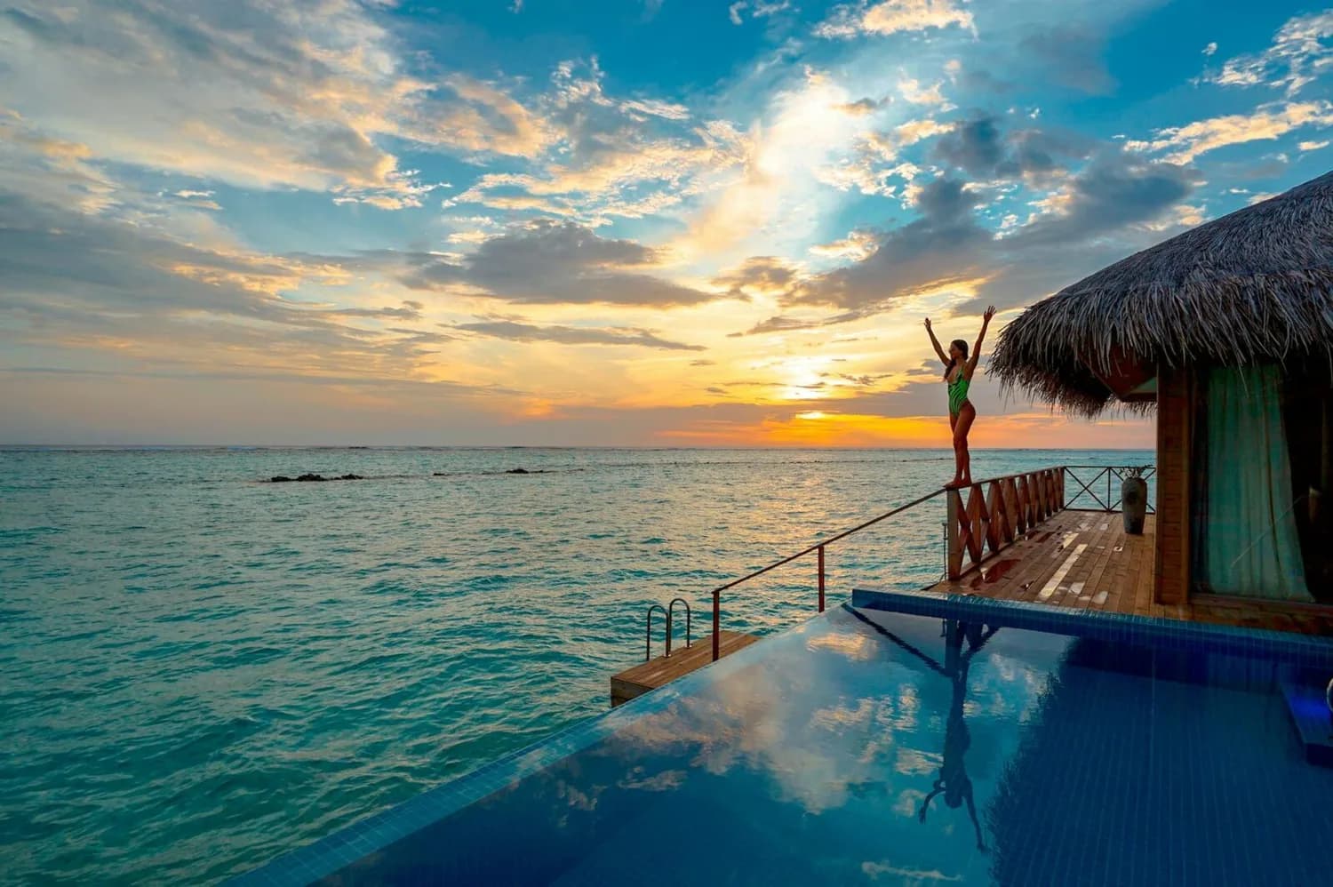 Frau im grünen Badeanzug auf Terrasse einer Overwater-Villa mit Infinity-Pool beim Sonnenuntergang über türkisfarbenem Meer auf den Malediven, ParkSleepFly-Flüge Erwähnung vermeiden?
