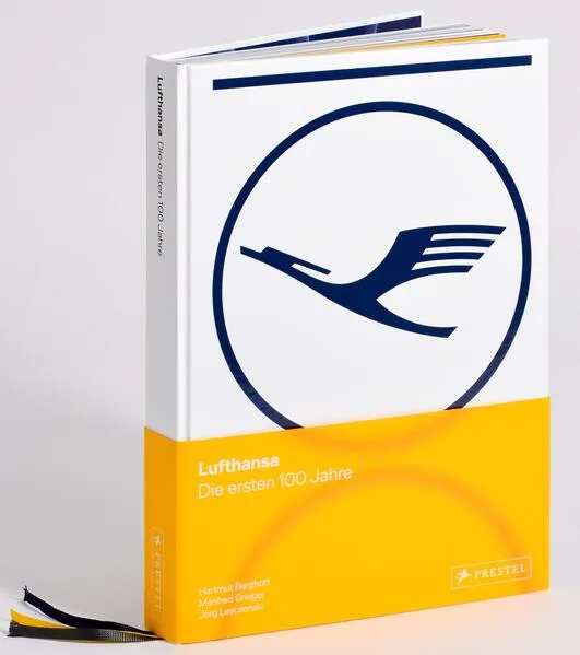 Aufgeschlagener Lufthansa-Bildband mit blauem Kranich-Logo auf weißem Umschlag und gelber Buchhülle, Jubiläumsband zu den ersten Unternehmensjahren