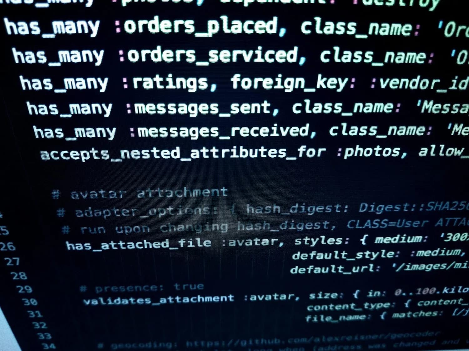 Zeigt Computerbildschirm mit Quellcode und Datenbank-Attributen; Schlüsselwörter wie has_many, orders_serviced, messages_received; Kontext IoT Jettainer Lufthansa Cargo nicht sichtbar aber relevant für Bildverwendung.