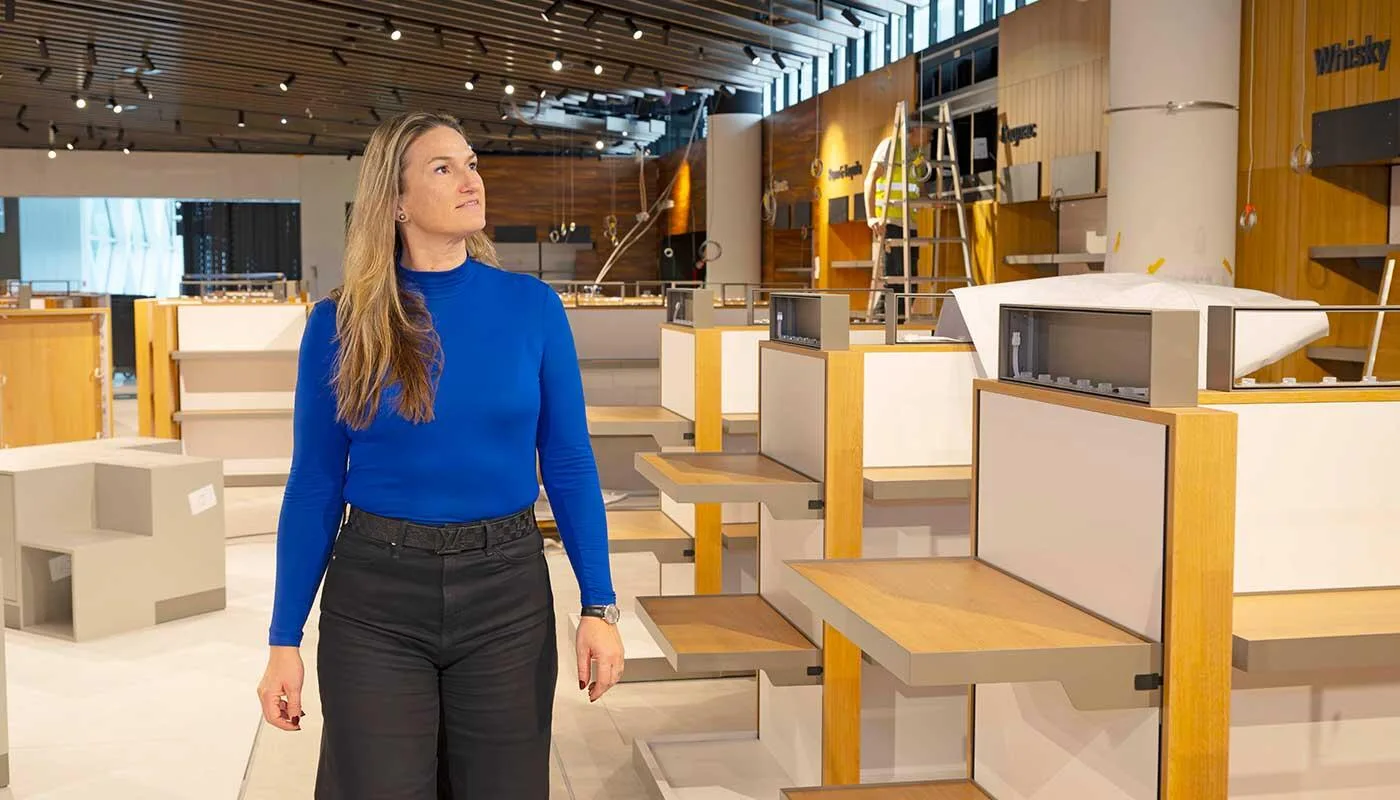 Frau in blauem Pullover in leerem Duty-Free-Shop am Flughafen München Terminal 1 Pier, Regale und Displays im Aufbau - Wenn aus Plänen langsam Realität wird: Elke Haeffner schaut nach dem Baufortschritt im neuen Duty-Free-Store im Terminal 1-Pier. Voller Vorfreude blickt sie auf die Shopping- und Gastronomiewelt, die im April eröffnet wird.