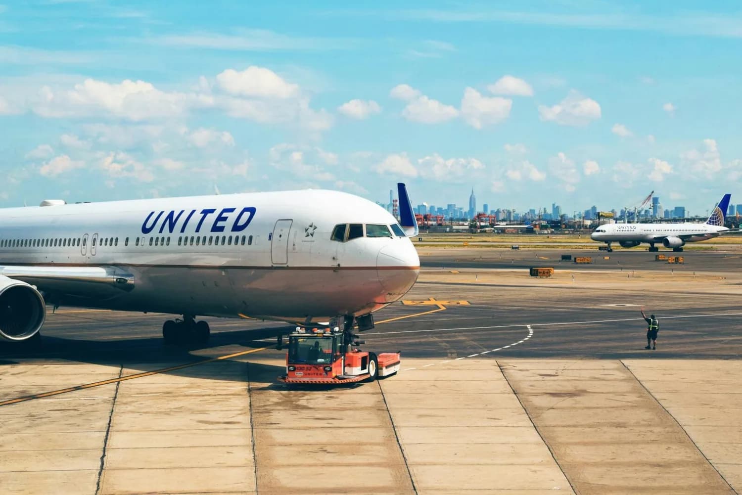 United Airlines Passagierflugzeug am Gate, Schlepper zieht Flugzeug auf Rollfeld mit weiter startender United-Maschine und Flughafenszene im Hintergrund