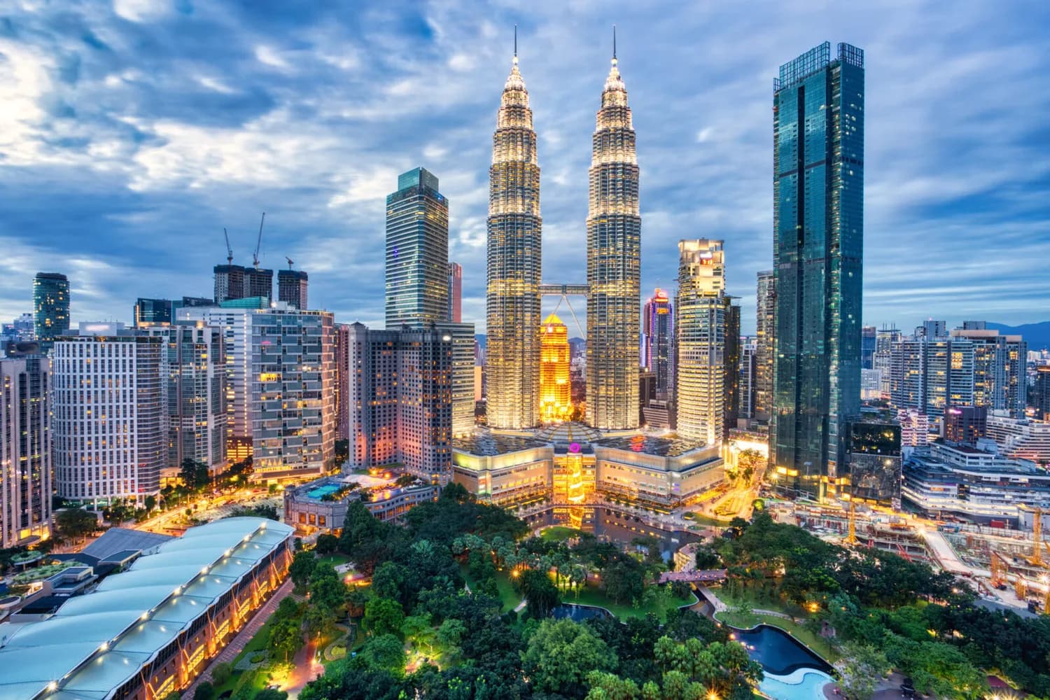 Kuala Lumpur Skyline mit beleuchteten Petronas Twin Towers, umliegende Wolkenkratzer und Park bei Dämmerung, städtische Architektur und Lufthansa-Verbindungshinweis (KUL)
