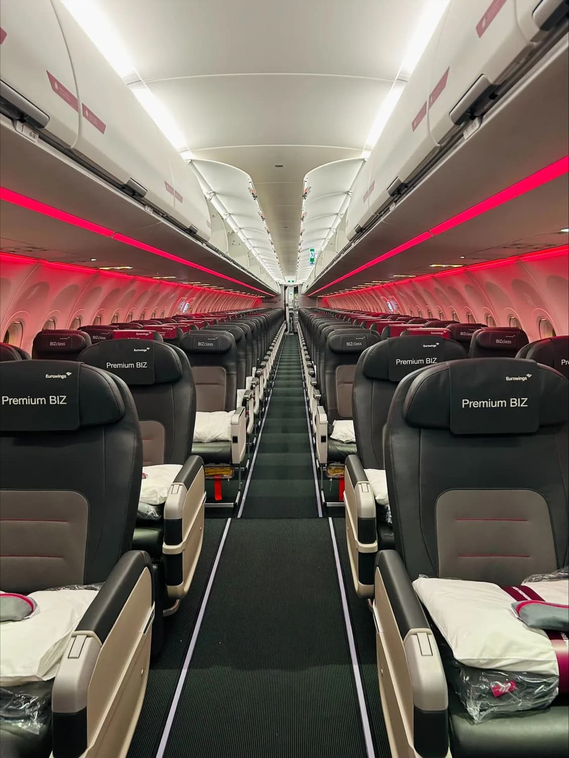 Innenansicht Eurowings Premium BIZ Kabine mit Reihen von Ledersitzen, Kopfstützenbeschriftung Premium BIZ und roter Kabinenbeleuchtung beim Erstflug BER–DXB