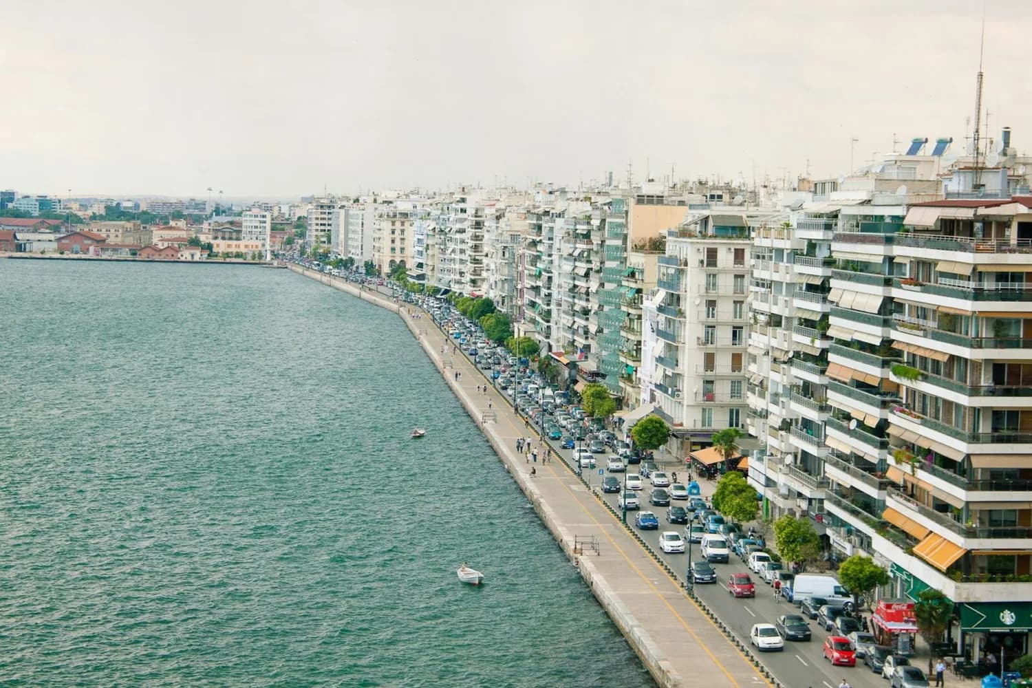 Promenade an der Uferstraße von Thessaloniki mit Reihenwohnhäusern, parkenden Autos und Fußgängern entlang des Meeresfronts