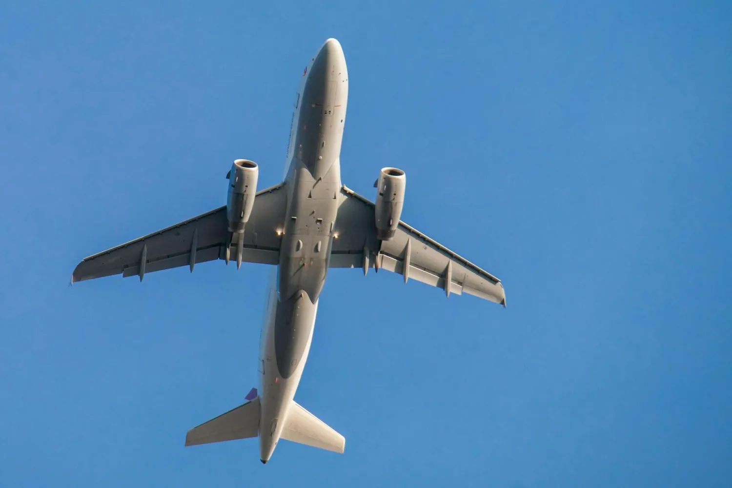 Passagierflugzeug SkyExpress von unten vor klarem blauen Himmel, Seitenruder und Triebwerke sichtbar