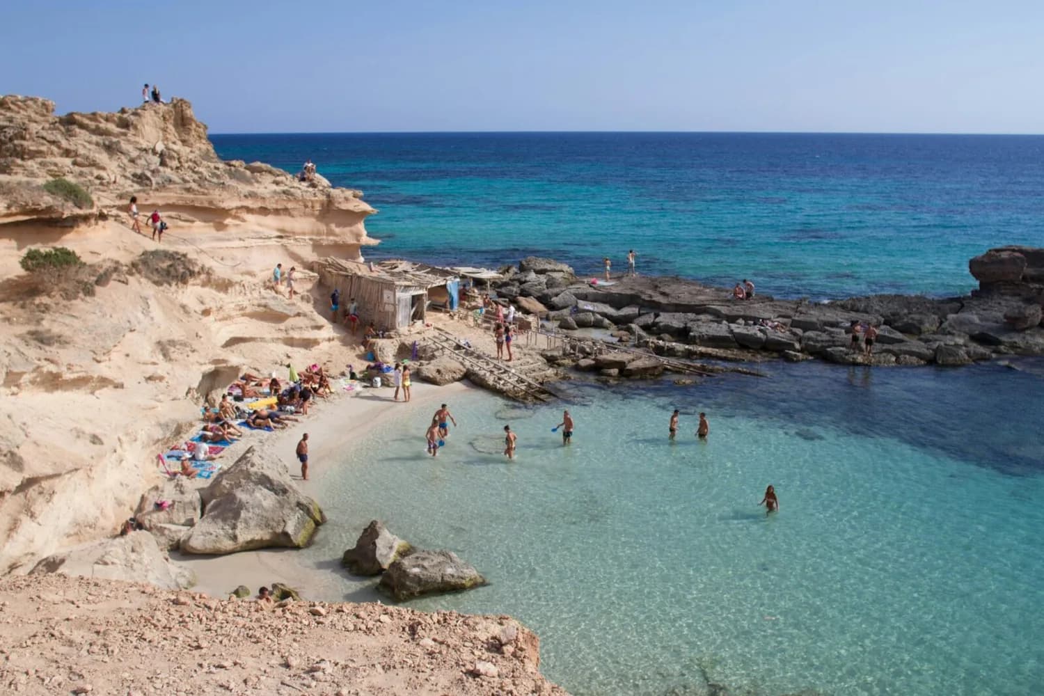Kleine Badebucht auf den Balearischen Inseln mit klar-türkisfarbenem Wasser, Sandstrand, Felsenklippen und Badenden am Ufer