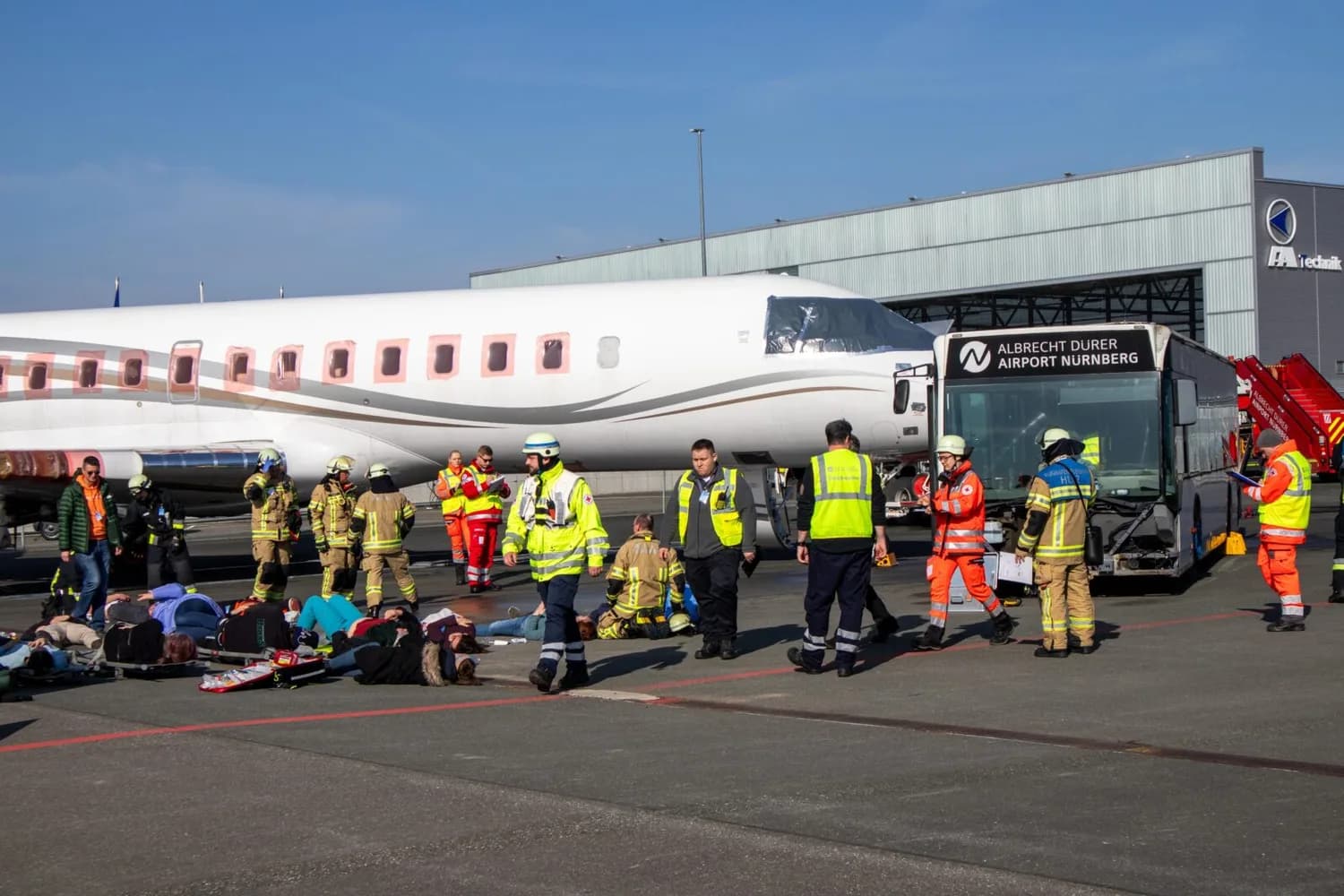 Rettungskräfte und Feuerwehr am Flughafen Nürnberg versorgen verletzte Passagiere auf dem Vorfeld neben einer Regionalmaschine und Flughafenbus mit Aufschrift Albrecht Dürer Airport Nürnberg