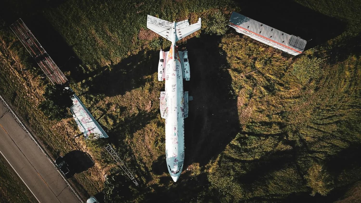 Draufsicht auf verlassenes Flugzeugwrack auf Grasland neben Straße, bemalte Rumpf- und Tragflächen, nahe abgestellter Reisebus und Fahrzeug – Symbolbild Ryanair faire Arbeitsbedingungen