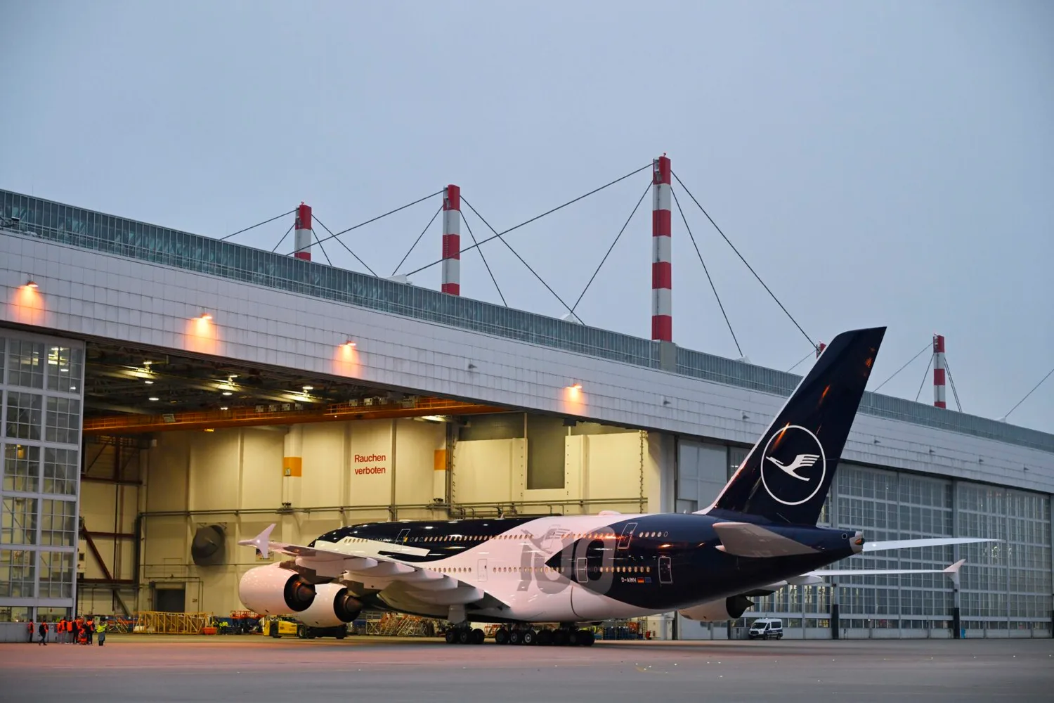 Lufthansa A380 mit Kranich-Logo parked vor Hangar bei Dämmerung, Bodenpersonal und Flughafeninfrastruktur sichtbar