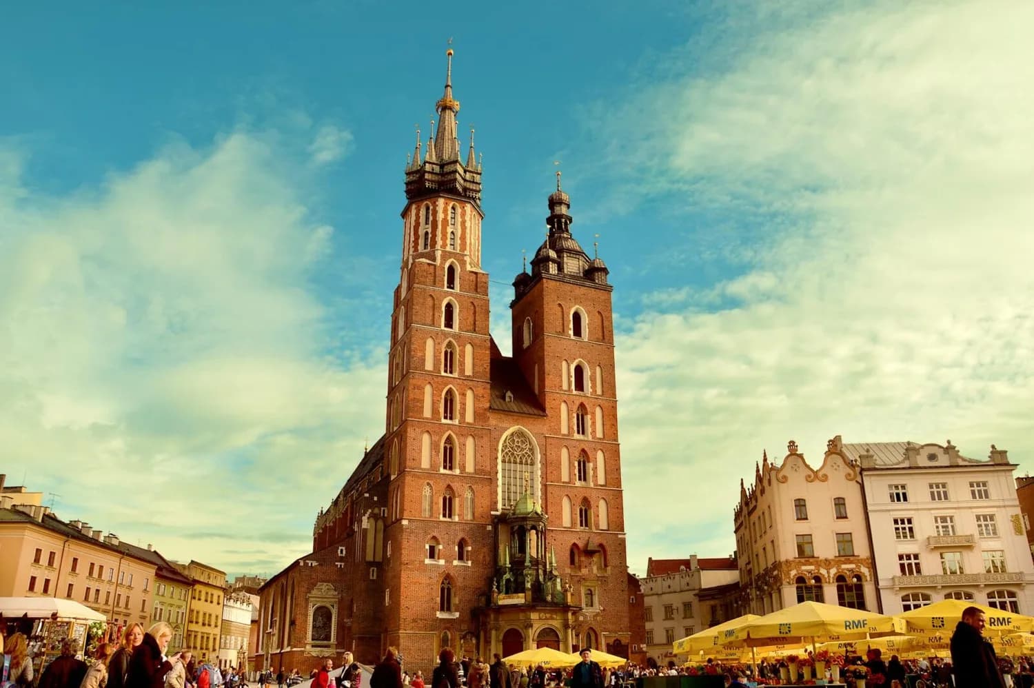 Mariä-Himmelfahrt-Kirche (St. Marys Basilica) am Marktplatz von Krakau mit zwei Türmen, umliegenden historischen Häusern und Menschen auf dem Platz