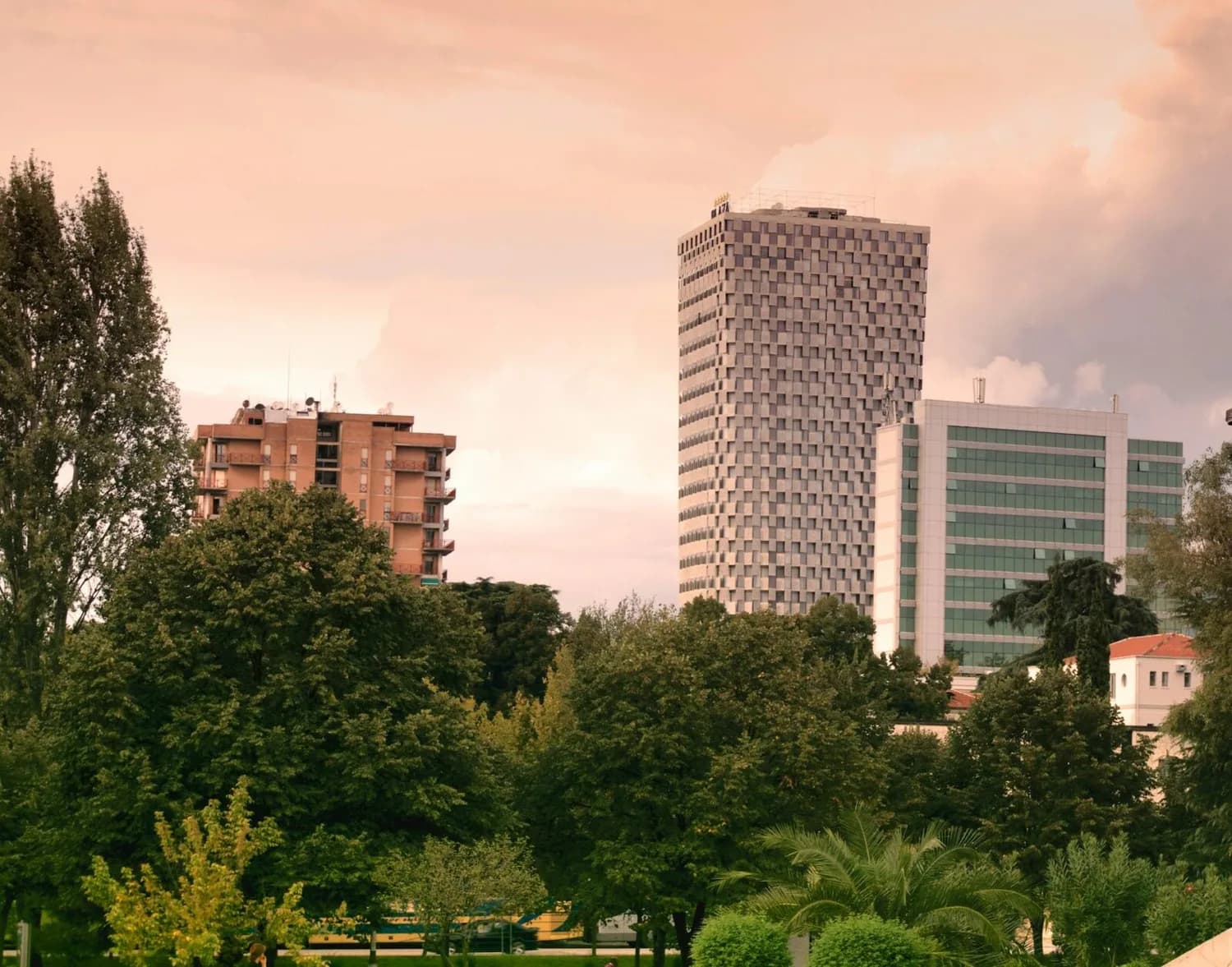 Stadtpanorama Tirana Albanien mit hochhäusern, modernem Büroturm, Wohngebäude und grünen Parkbäumen bei warmem Himmel