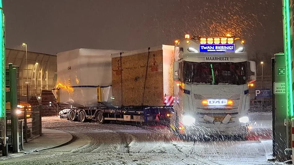 Lkw mit Schwertransport und verpackter Boeing‑777‑Simulatorladung bei Schneefall am Flughafen Frankfurt, beleuchteter Truck von Twan Bierings auf verschneiter Zufahrt