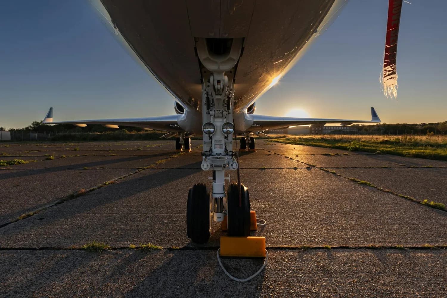 Bugfahrwerk eines geparkten Verkehrsflugzeugs bei Sonnenuntergang auf dem Vorfeld des Flughafens Memmingen, AllFuel-Tankstelle im Hintergrund