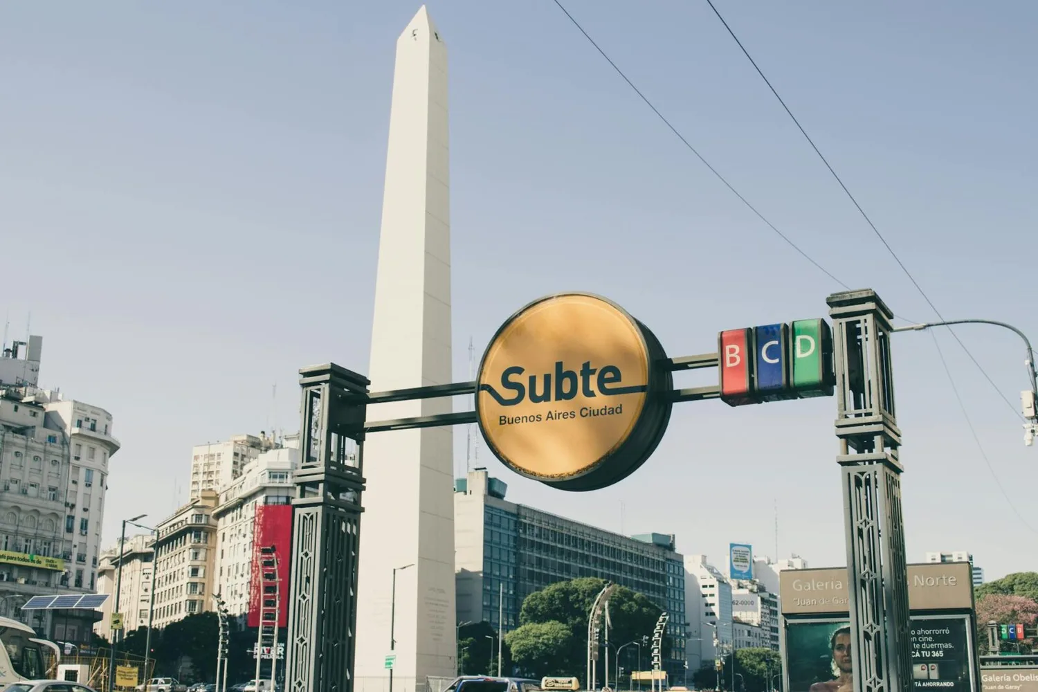 Eingang zur Subte U-Bahn mit gelbem Subte-Schild vor dem Obelisk von Buenos Aires, städtische Gebäude und Straßenverkehr in Argentinien