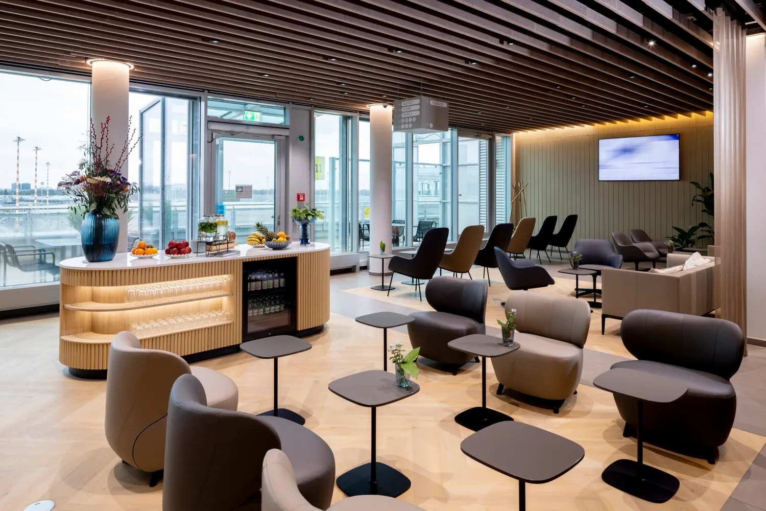 Moderne Flughafenlounge DUS mit bequemen Sesseln, kleinen Tischen, Buffet mit Obst und Getränken, großer Fensterfront zum Vorfeld und entspannter Atmosphäre - Foto: Andreas Wiese