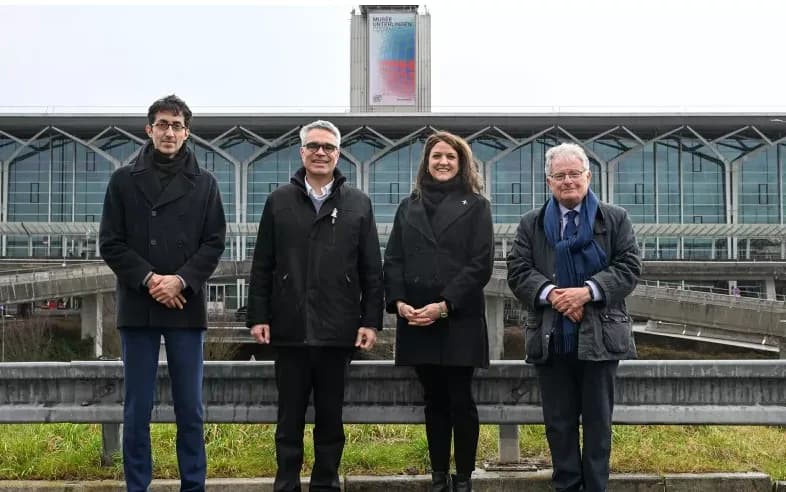 Vier Personen in Wintermänteln stehen vor dem EuroAirport-Terminal mit sichtbar angebrachtem Victor-Vasarely-Banner auf der Fassade