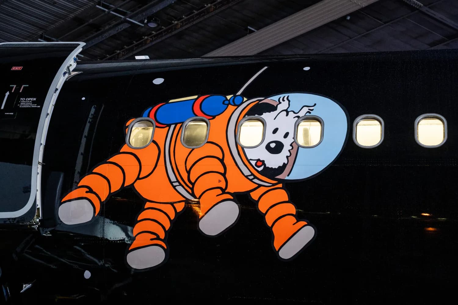 Brussels Airlines Flugzeugseite mit großem bunten Aufkleber von Tim und Struppi‑Figur Captain Haddock in orangem Raumanzug neben Fensterreihe - © Brussels Airlines / Hergé / Tintinimaginatio 2026