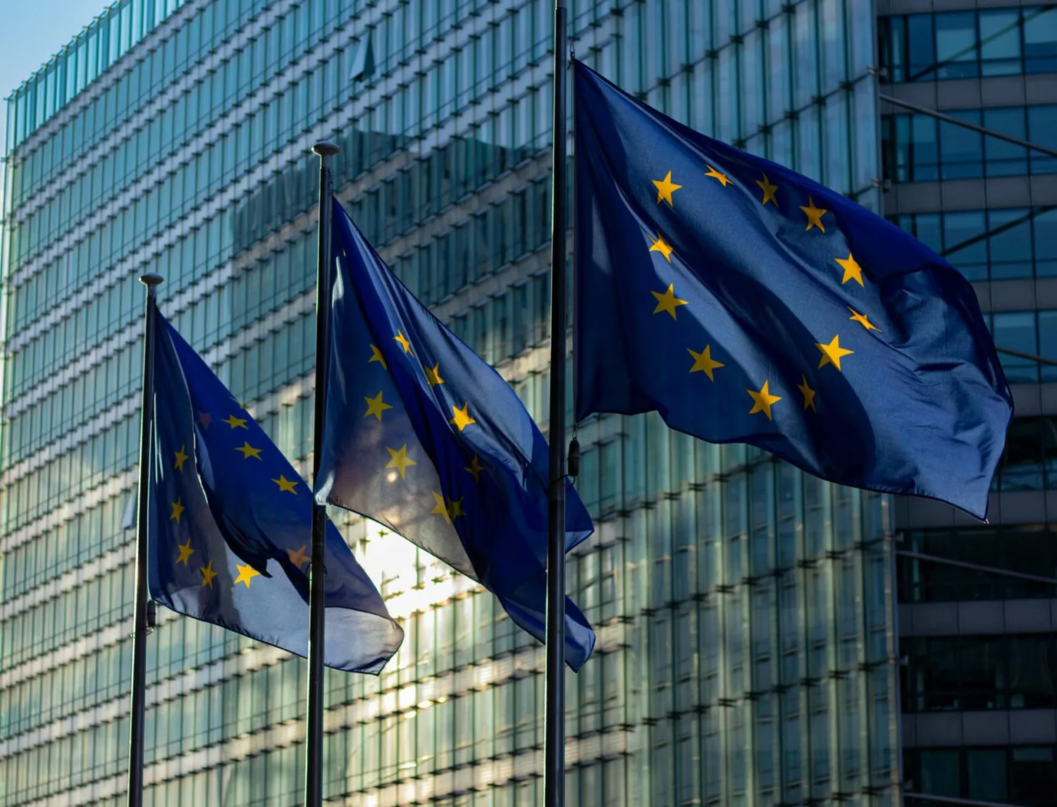 Drei wehende EU-Flaggen vor gläsernem Verwaltungsgebäude symbolisieren EU-Reform und Regelungsänderungen