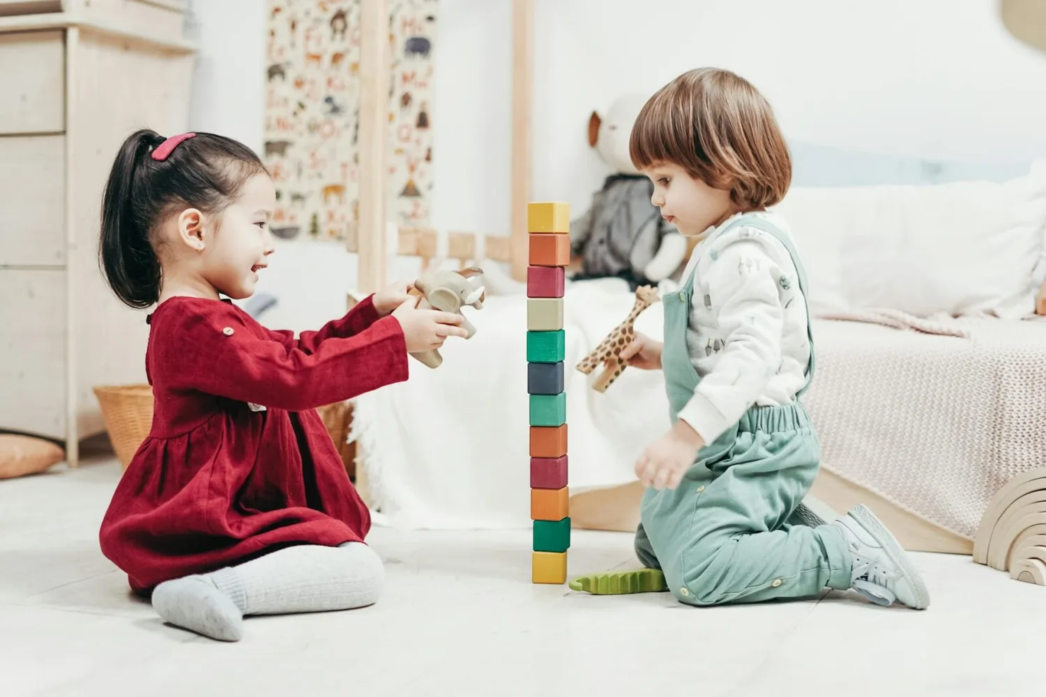 Zwei Kleinkinder in Kita am Flughafen München spielen mit bunten Holzbausteinen und Tierfiguren auf dem Boden