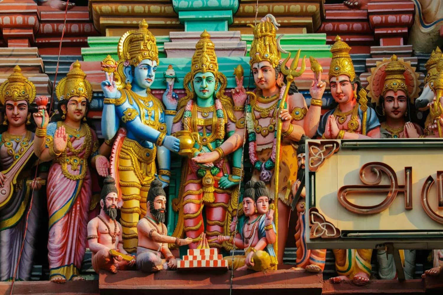 Bunte Skulpturen hinduistischer Götter und Priester an der Fassade eines indischen Tempels