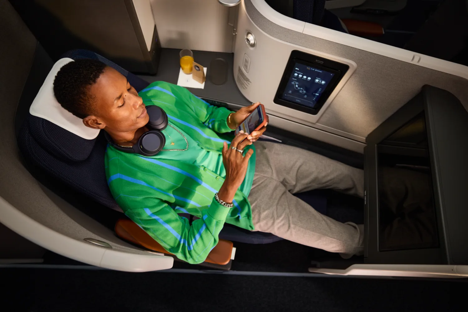Passagier entspannt in Lufthansa Business Class Allegris Suite mit Kopfhörern, Touchscreen, Getränk und Smartphone