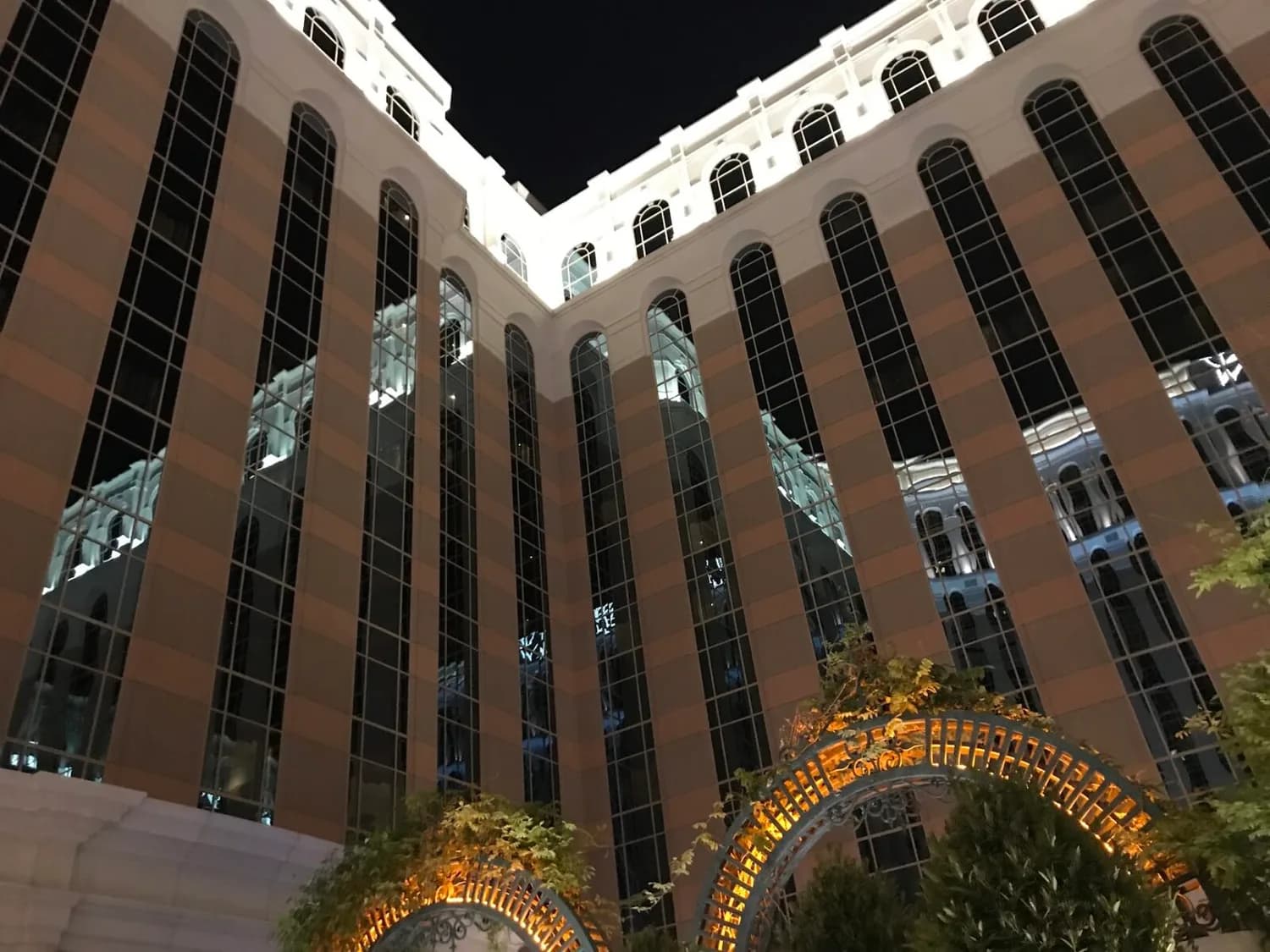 Außenansicht eines beleuchteten Luxushotels in Las Vegas mit hohen bogenförmigen Fensterreihen und beleuchteter Garten-Architektur im Vordergrund