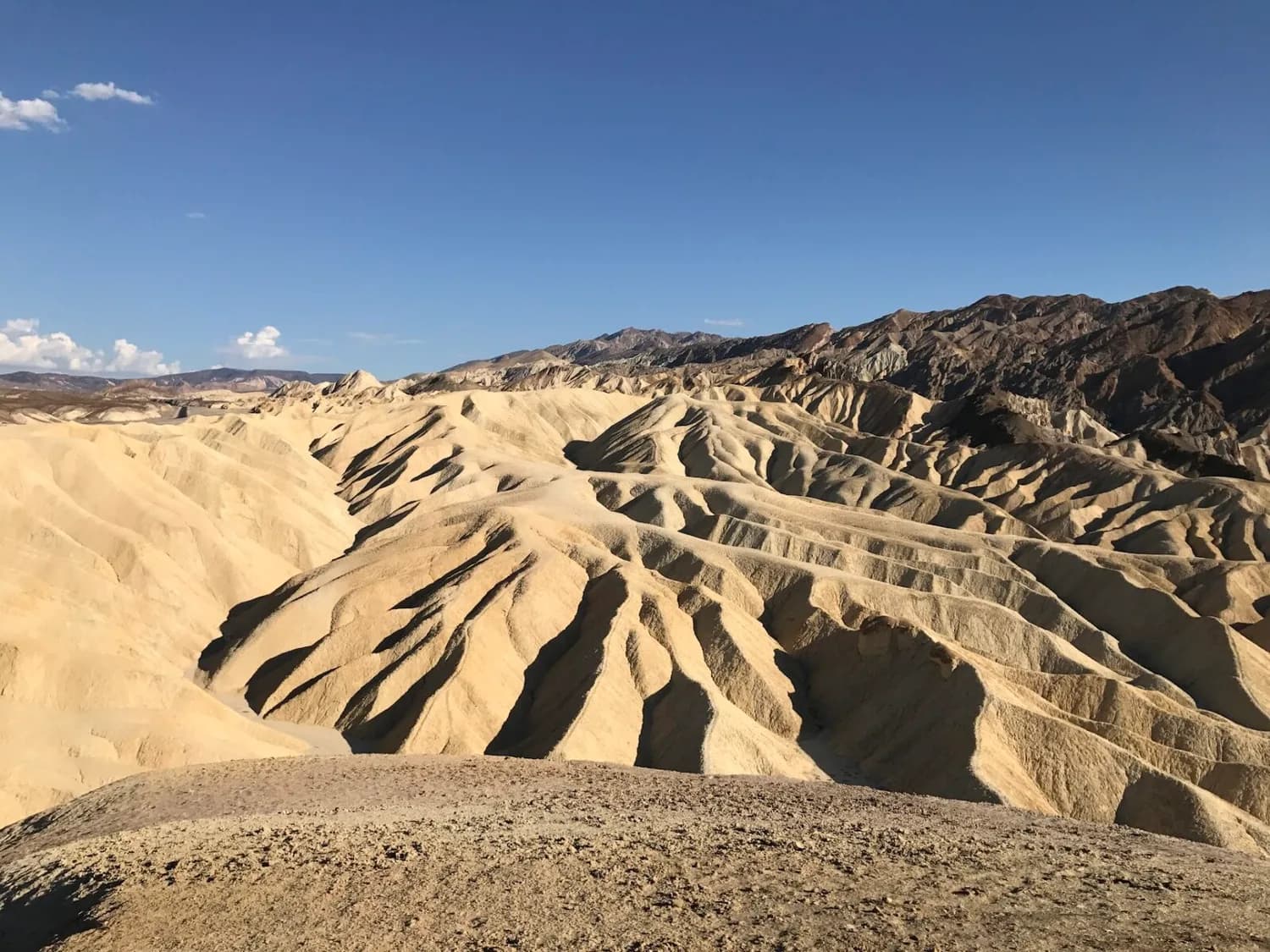 Trockene, zerfurchte Badlands-Landschaft im Death Valley, Nevada mit sandfarbenen Hügeln und blauem Himmel