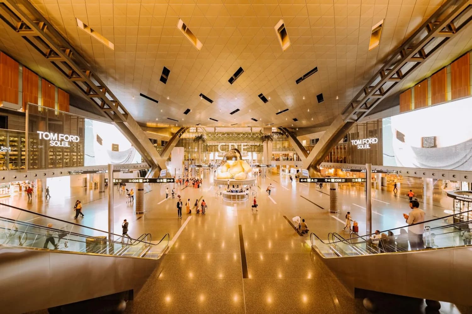 hell beleuchtete futuristische Flughafenhalle in Doha, mit großer Skulptur in der Mitte, Reisende, Rolltreppen, Duty-Free-Shops und digitale Werbetafeln, moderne Architektur und weitläufiger Check-in-Bereich