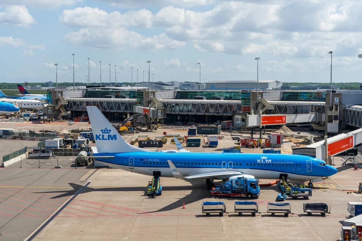 KLM-Passagierflugzeug am Gate am Flughafen Amsterdam Schiphol mit Boardingbrücken, Bodenfahrzeugen und Gepäckwagen vor dem Terminal