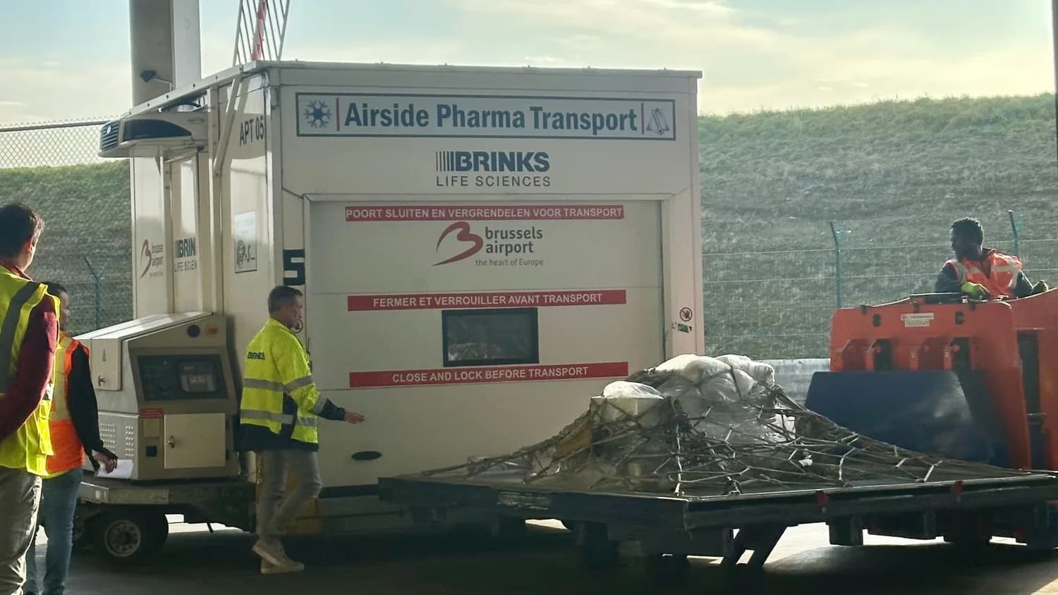 Spezialcontainer von Brinks Life Sciences für pharmazeutischen Transport am Flughafen Brüssel, Flughafenpersonal beim Verladen von Krebsbehandlungsmedikamenten und Frachtpalette mit Netzung