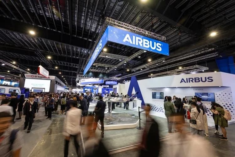 Messehalle mit Besucherinnen und Besuchern am Airbus-Messestand, Ausstellungsflächen, Modellpräsentationen und großem beleuchteten Airbus-Logo über dem Stand