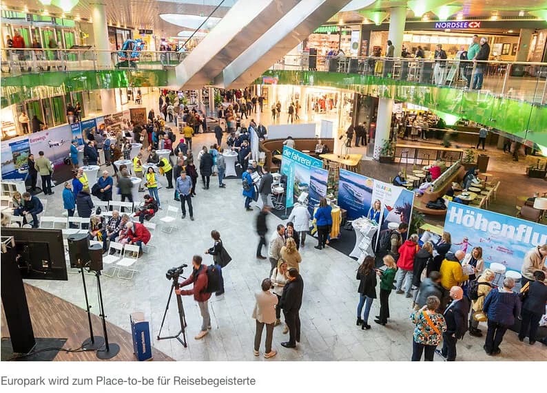 Menschen auf Reisemesse im Einkaufszentrum Europark Salzburg mit Informationsständen, Besuchern und Bühne in heller Mall-Atmosphäre