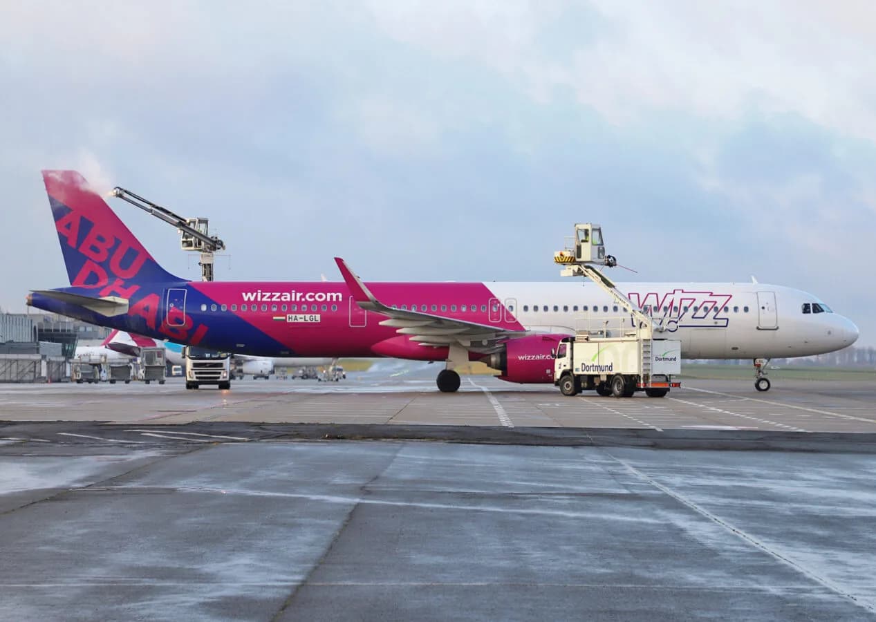 Wizz Air Passagierflugzeug wird am Flughafen Dortmund enteist, Enteiserfahrzeug mit Hebebühne arbeitet an Tragfläche und Heck, pink-violettes Flugzeug mit Abu Dhabi Schriftzug