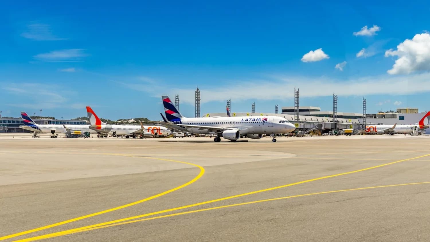 Flugzeug von LATAM auf dem Vorfeld eines Flughafens mit geparkten Flugzeugen der Airlines GOL und LATAM, Terminalgebäude und blauem Himmel