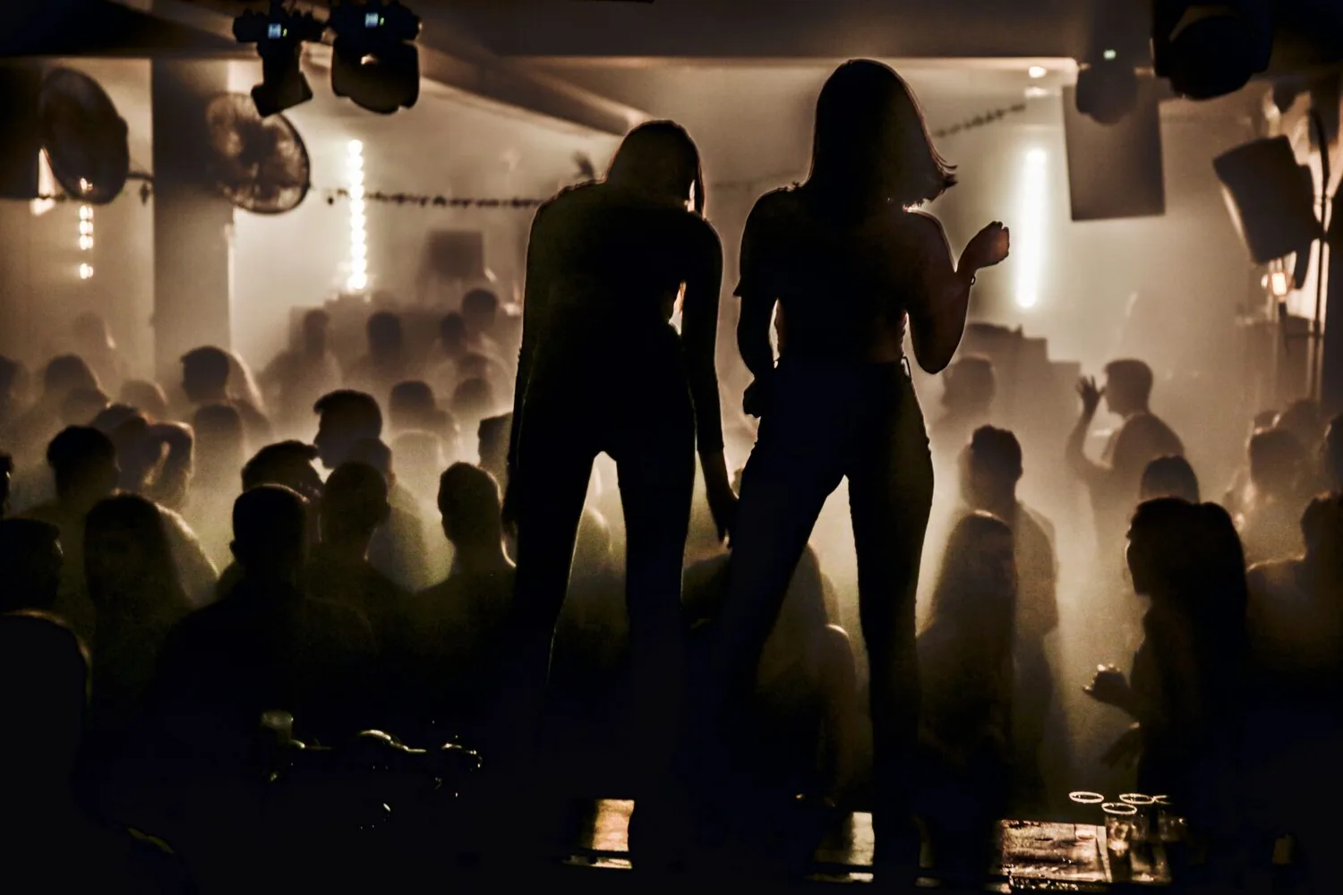 Dunkles Nachtclub-Interior mit tanzender Menschenmenge und zwei silhouetten auf einer Bühne, stimmungsvolle Beleuchtung und Nebel, Party-Atmosphäre und DJ-Club-Szene