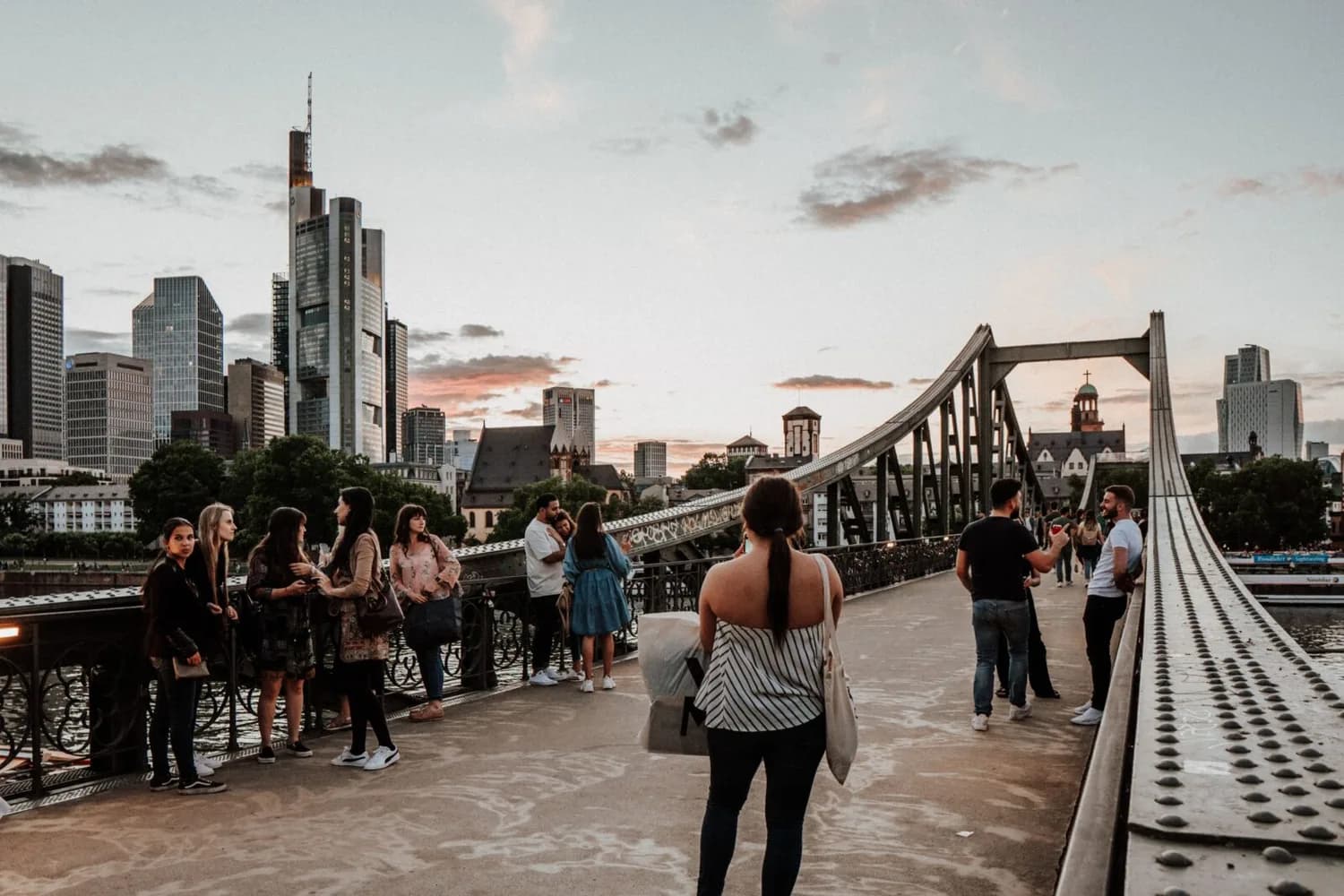 Fussgänger auf der Eisernen Steg Brücke vor Frankfurter Skyline bei Sonnenuntergang, Menschen beim Spazieren und Fotografieren, städtische Sehenswürdigkeit für Städtereisen Top Ten