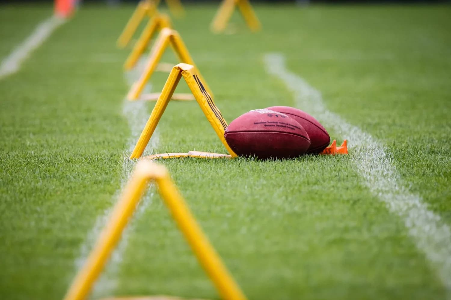NFL Footballs auf Rasen neben gelben Trainingshürden und Feldmarkierung beim American-Football-Training