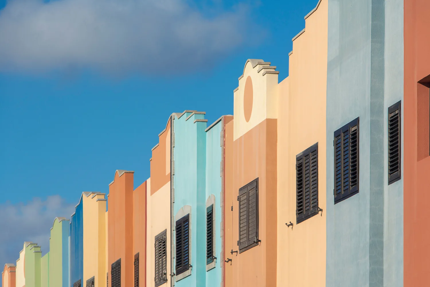 Bunte koloniale Häuserfassaden in Willemstad, Curaçao, mit pastellfarbenen Giebeln und dunklen Fensterläden unter blauem Himmel