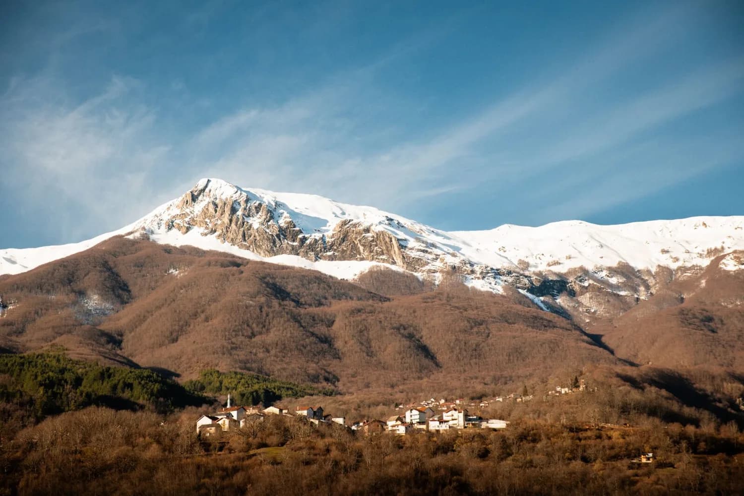 Dorfgemeinschaft unter verschneitem Berggipfel bei Radostusha, Nordmazedonien – Panoramablick auf Waldhänge und traditionelle Häuser