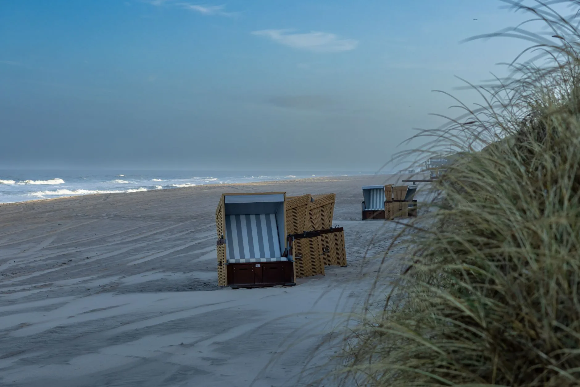 Leere Strandkörbe am menschenleeren Nordseestrand mit Dünengras im Abendlicht