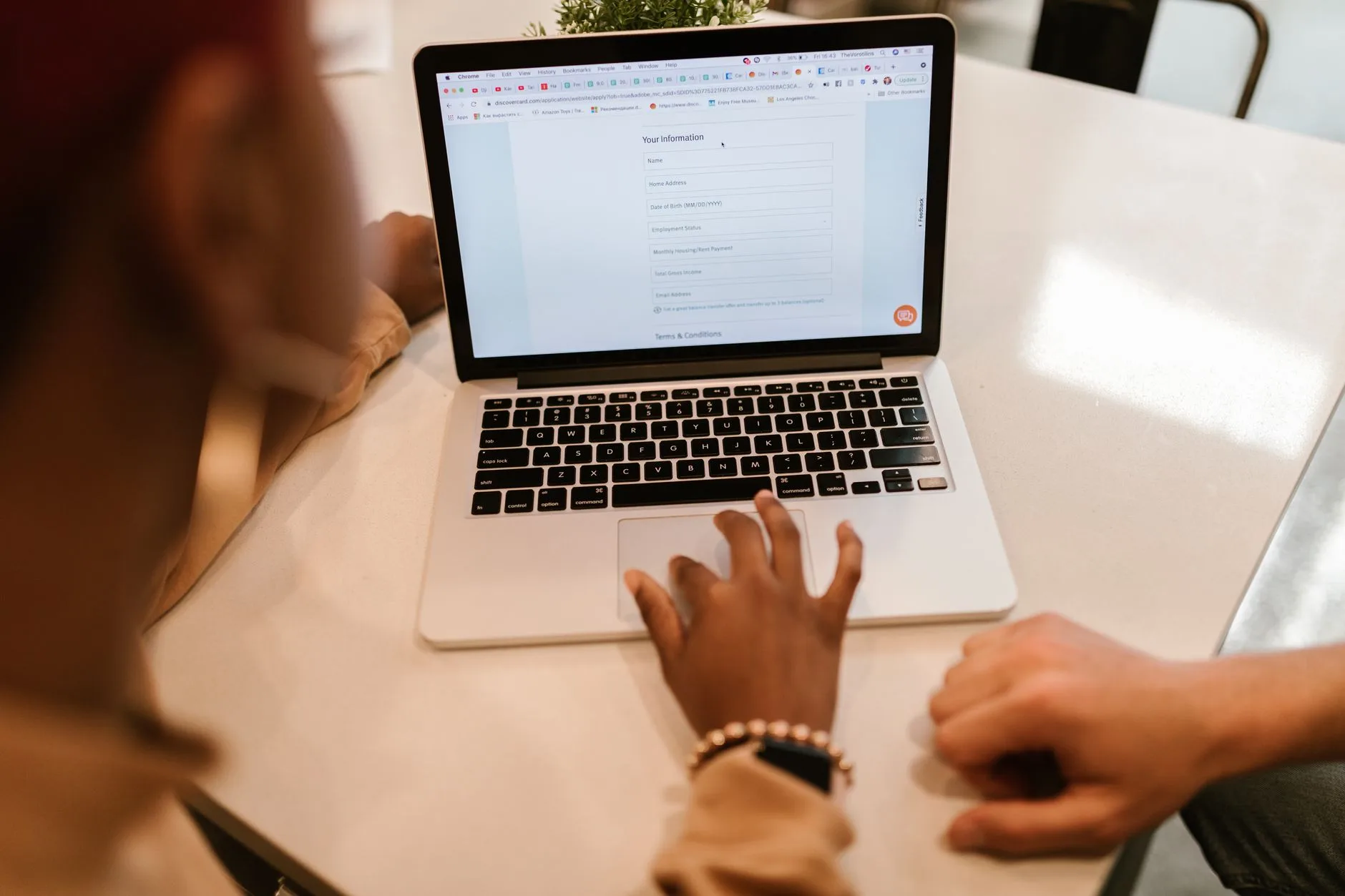 Person tippt auf Laptop-Trackpad, Bildschirm zeigt Online-Formular mit persönlichen Angaben